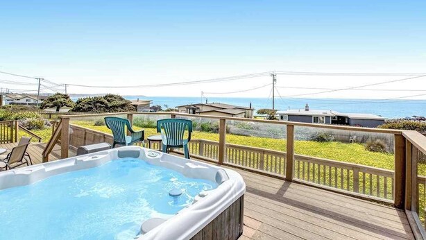 A hot tub on a wooden deck with chairs, overlooking a grassy area and a view of the ocean. - Bodega Bay 3BR ocean-view cottage with hot tub — dogs welcome (Bodega Bay)