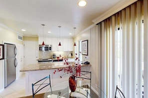 A modern kitchen with a central island, stainless steel appliances, pendant lighting, and a glass dining table with chairs. - Napa 1BR Silverado Trail condo with fireplace, pool & EV charger (Napa)
