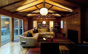 A cozy cabin interior with a wooden ceiling, a sectional sofa, a fireplace, and a bookshelf. - Forestville 3BR redwood cabin with gas fireplace, fire pit & deck (Forestville)