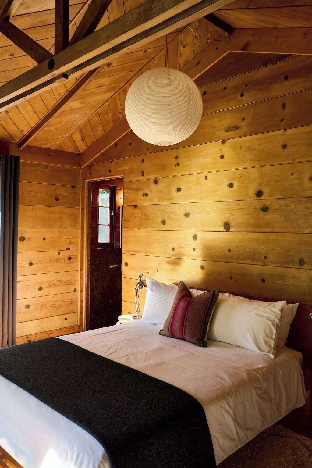 A wooden cabin bedroom with a bed, pillows, a nightstand, and a hanging light fixture.