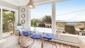 A dining area with a glass table and chairs, a hanging light fixture, and a view of the outdoors.