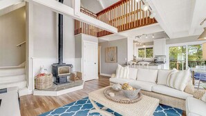 A spacious living area with a fireplace, a white sofa, and a kitchen in the background.