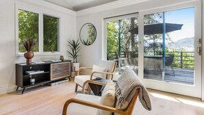 Uma sala de estar espaçosa com uma grande porta de vidro deslizante que dá para um deck externo, uma lareira moderna e decoração de estilo minimalista.