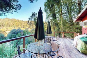 A deck with outdoor furniture, a bed, and a view of a forested area.