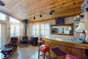 A cozy cabin interior with a wooden ceiling, a fireplace, a bar area, and a large mirror.