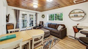 Un salon chaleureux avec un plafond en bois, une table basse ronde, un canapé et une fenêtre donnant sur un paysage verdoyant.