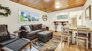 Un salon avec un plafond en bois, un canapé, une table basse, une table à manger avec des chaises et un tapis.