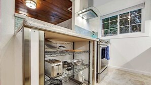 Une cuisine de taille réduite, dotée d’appareils électroménagers intégrés, d’une fenêtre et d’un plafond en bois.