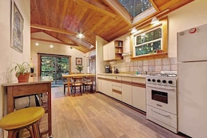 A kitchen with wooden ceiling beams, a dining area with chairs, a stove, and a refrigerator.