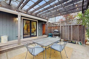 A patio with a table and chairs, a grill, and a wooden fence.