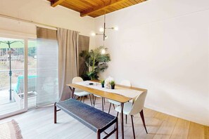 A dining area with a wooden table, white chairs, a bench, and a potted plant.