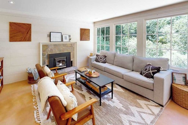Sink into your sun-drenched living room where a stone fireplace, plush seating, and walls of windows frame the surrounding redwood canopy — your Guerneville escape starts here.