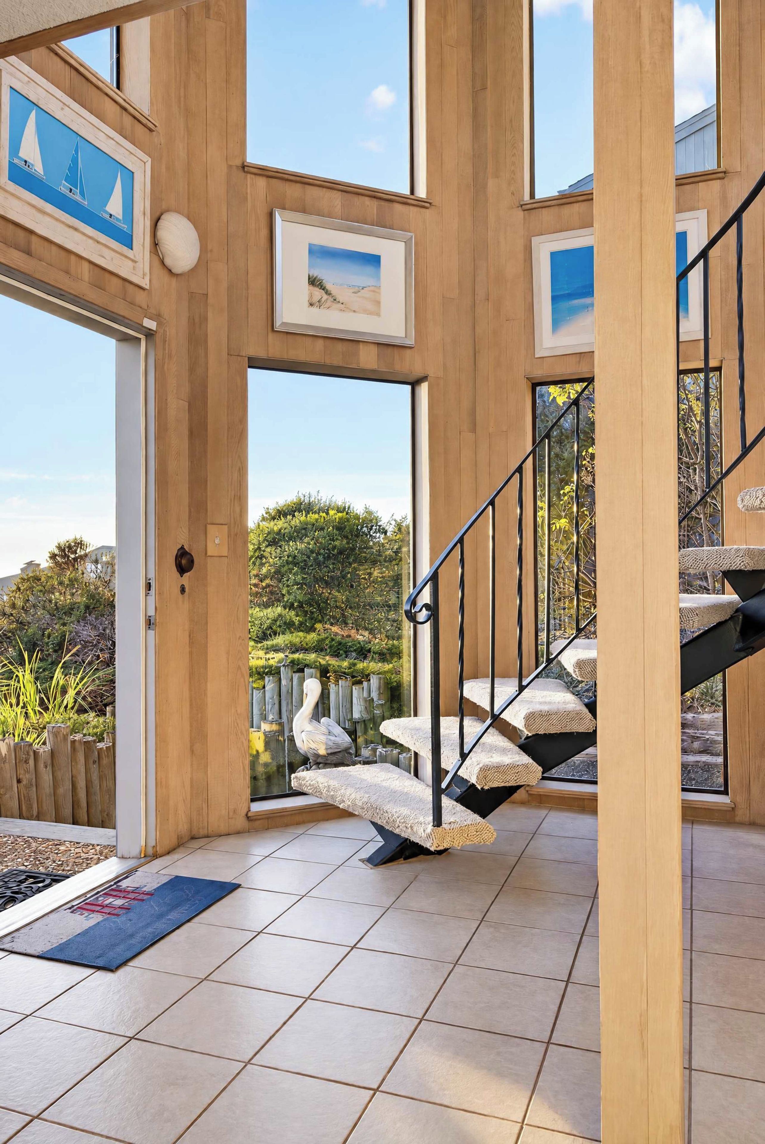 A spacious interior with wooden walls, a staircase with cushioned steps, and large windows offering views of the outdoors.