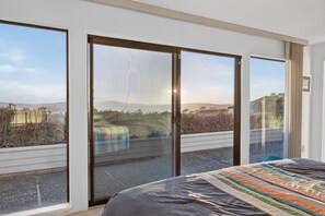 A bedroom with a large bed, a view of a balcony, and a sliding glass door leading to an outdoor area. - Bodega Bay 3BR ocean-view home with game room and two king beds (Bodega Bay)