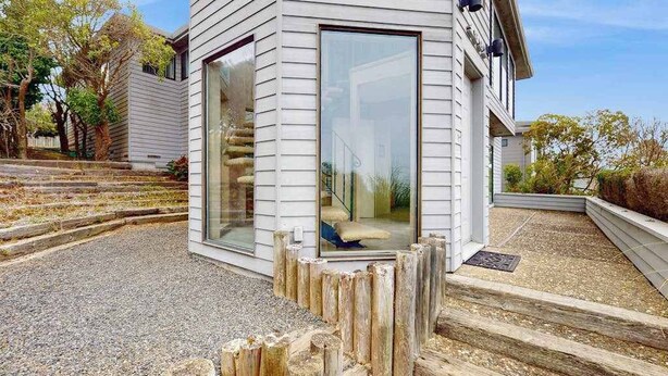 Una casa moderna con un'ampia vetrata, un patio in legno e un vialetto sterrato.