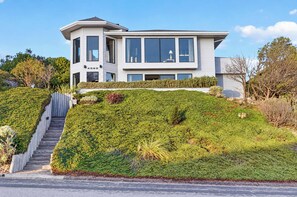 A modern two-story house with a large balcony, a staircase leading up to the entrance, and a well-maintained garden. - Bodega Bay 3BR ocean-view home with game room and two king beds (Bodega Bay)