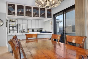 A modern kitchen with white cabinets, a dining table with chairs, and a large window with a view. - Bodega Bay 3BR ocean-view home with game room and two king beds (Bodega Bay)