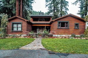 A log cabin with a stone foundation, a central entrance, and a stone pathway leading to the door.