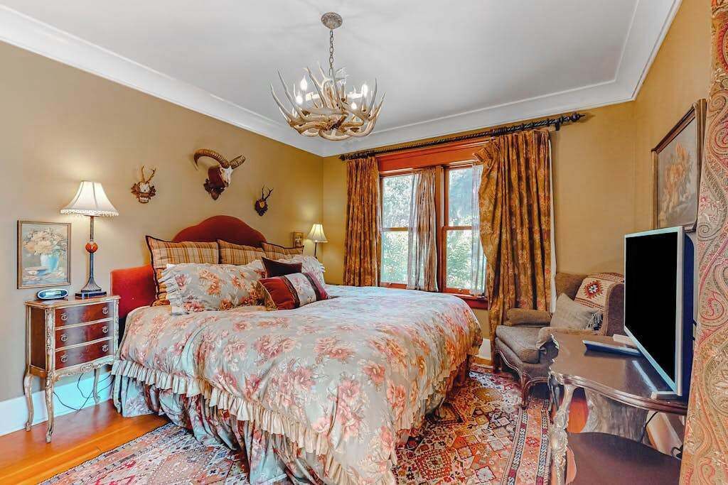 Une chambre à coucher avec un grand lit, un lustre, une télévision et une fenêtre avec des rideaux.