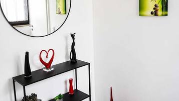 Ein modernes Interieur mit einem runden Spiegel, einem schwarzen Konsolentisch mit Dekorationselementen, roten Vasen und zwei gerahmten Kunstwerken an der Wand.