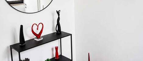 A modern interior with a round mirror, a black console table with decorative items, red vases, and two framed artworks on the wall.