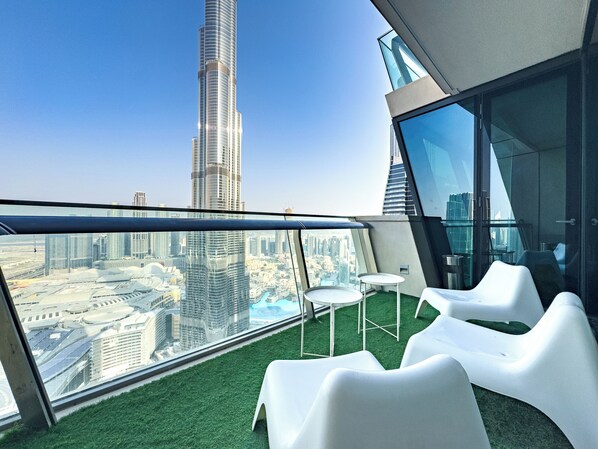 A high-rise building with a view of a tall skyscraper, a glass railing, and white chairs on a green surface. -     3BR Burj Khalifa View with balcony (Dubai)
