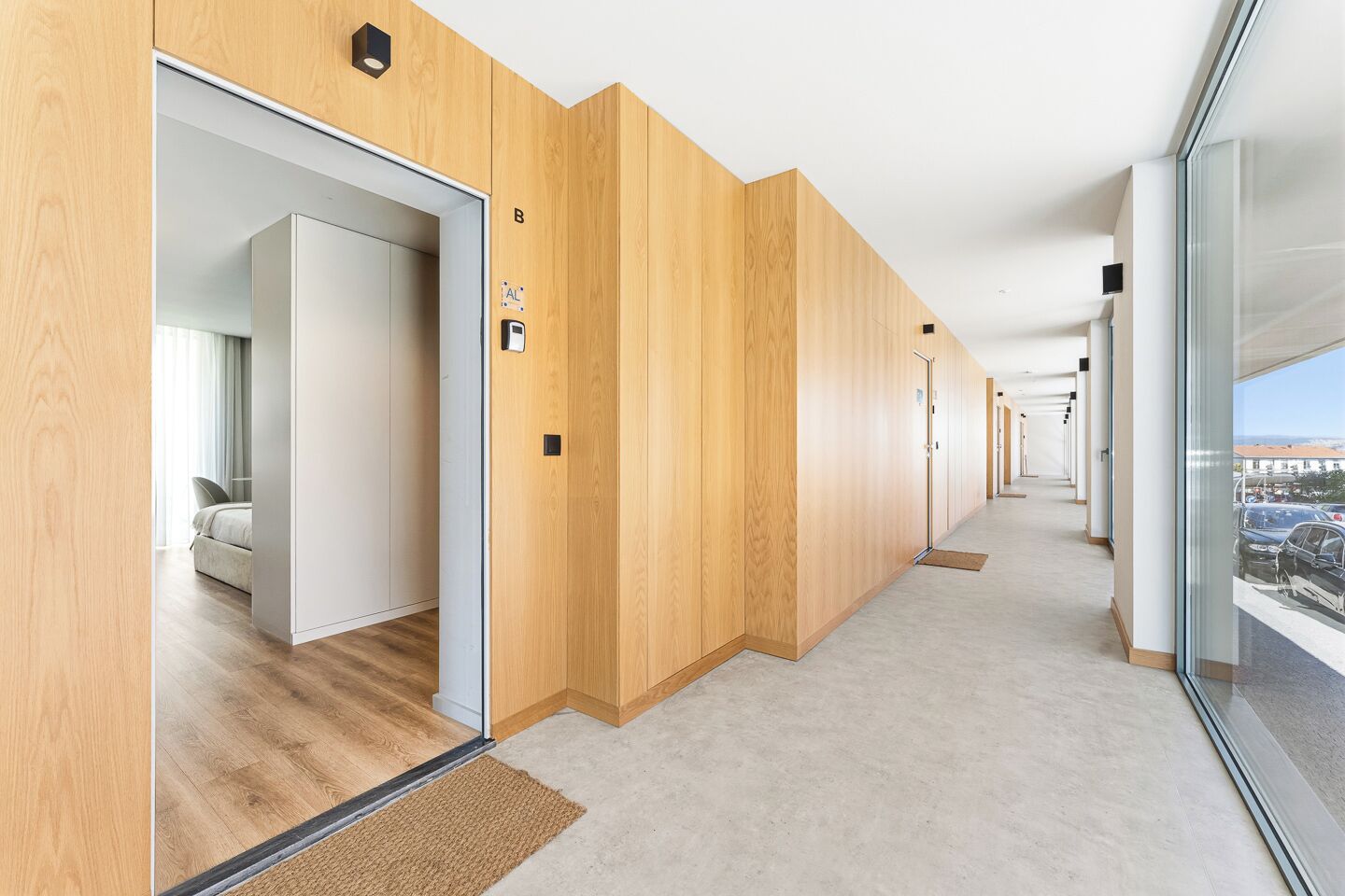 Ein Korridor mit Holzvertäfelung, eine Tür zu einem Zimmer mit einem Bett und ein Blick auf geparkte Autos vor dem Haus.