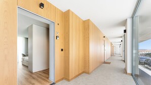 Ein Korridor mit Holzvertäfelung, eine Tür zu einem Zimmer mit einem Bett und ein Blick auf geparkte Autos vor dem Haus.
