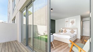 Ein modernes Schlafzimmer mit einem großen Bett, einer Glastür, die auf einen Balkon führt, und einer kleinen Sitzecke.