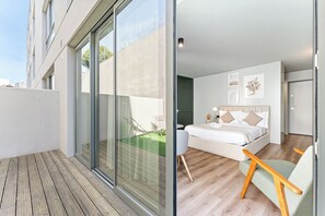 A modern bedroom with a large bed, a glass door leading to a balcony, and a small seating area. - The Telhado Studio | Modern Gaia Stay (Vila Nova de Gaia)