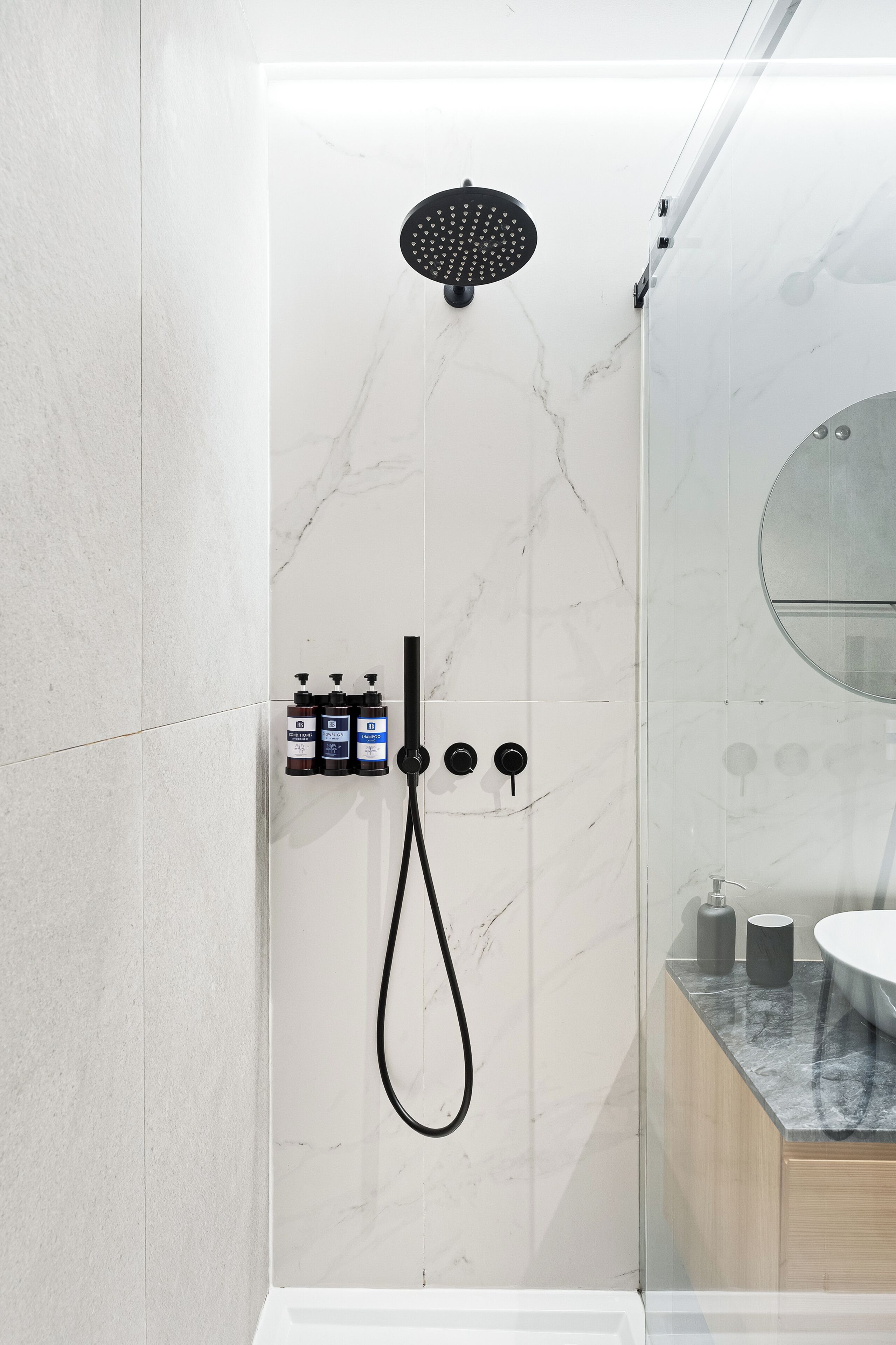 Ein modernes Badezimmer mit Dusche, Marmorwänden und einem runden Spiegel.