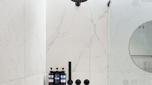 Ein modernes Badezimmer mit Dusche, Marmorwänden und einem runden Spiegel.