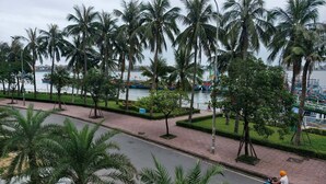 A coastal road lined with palm trees and a view of boats on the water. - July Hotel Quang Binh (Dong Hoi)