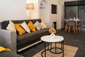 Ein modernes Wohnzimmer mit einer grauen Couch, einem runden Couchtisch und einem Essbereich mit Tisch und Stühlen.
