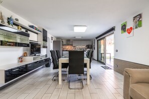 Uma cozinha moderna com armários brancos, uma área de jantar com mesa e cadeiras, e um sofá em primeiro plano.