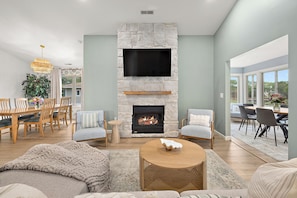 A living room with a stone fireplace, a flat-screen TV, and a dining area with wooden furniture.