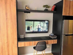 Eine moderne Küche mit integriertem Fernseher, Holzschränken, einem schwarzen Stuhl und einer kleinen Pflanze auf der Arbeitsplatte.