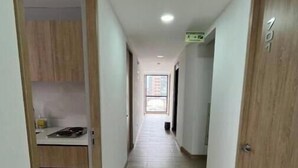 Un pasillo estrecho con suelo de madera, una zona de cocina a la izquierda y una puerta a la derecha.