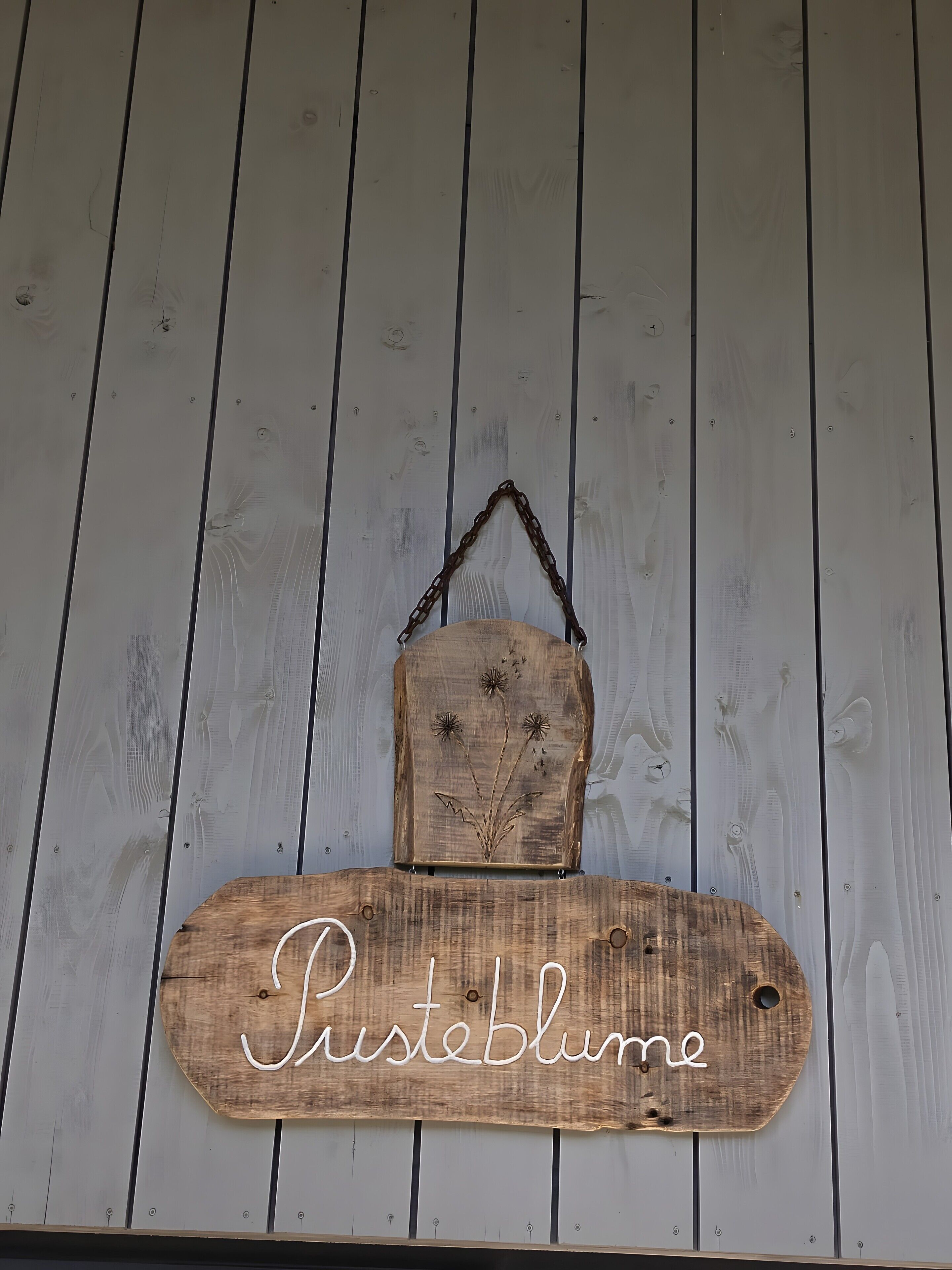 A wooden sign with the text 'Pusteblume' mounted on a wall with vertical wooden planks.