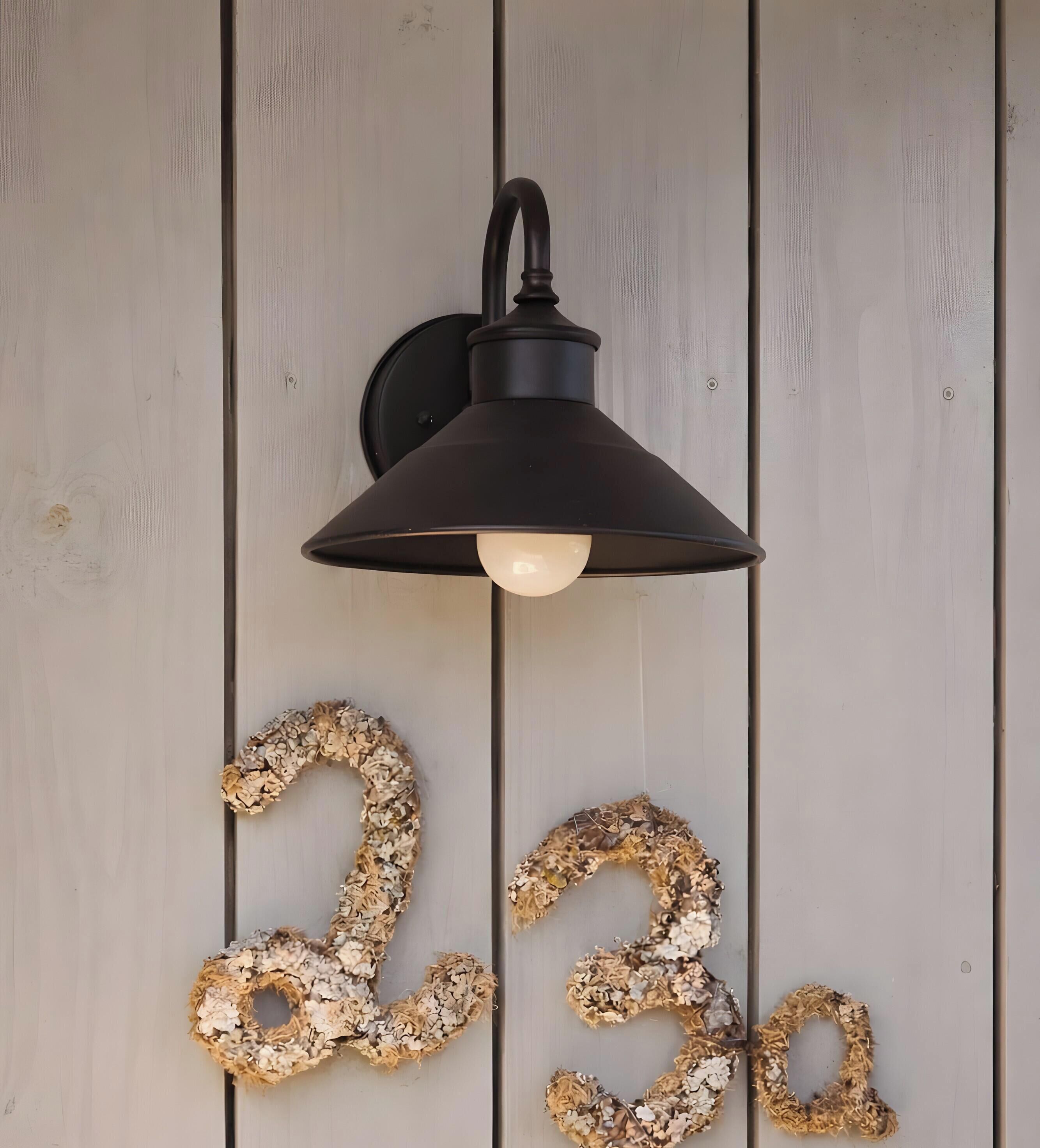 Une lampe noire fixée au mur, dotée d’une ampoule à lumière blanche, et ornée de chiffres décoratifs « 23 » fabriqués à partir de matériaux naturels.