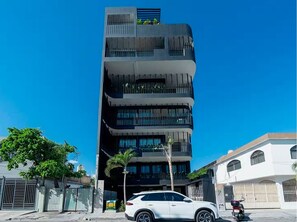 A multi-story building with balconies and a white car parked in front. - Modern 2BR Condo - Rooftop Pool + Prime Location (Playa del Carmen)