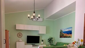 Ett vardagsrum med en TV, en soffa, ett matbord, stolar och en kristallkrona.