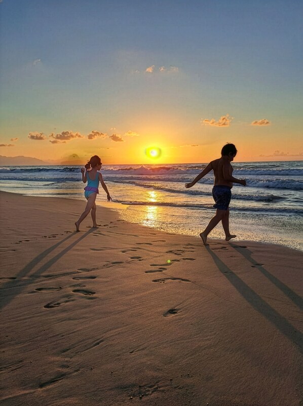Eine Strandansicht mit Fußspuren, die zum Meer führen, bei Sonnenuntergang.