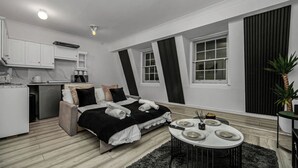 Ein modernes, kompaktes Hotelzimmer mit Bett, Esstisch, einer kleinen Küchenzeile und einem großen Fenster.