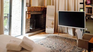 Quarto com cama, lareira, espelho grande, televisão e estante de livros.