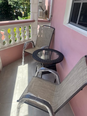Ein Balkon mit zwei Korbstühlen, einem Glastisch, einer rosafarbenen Wand und einem Fenster.