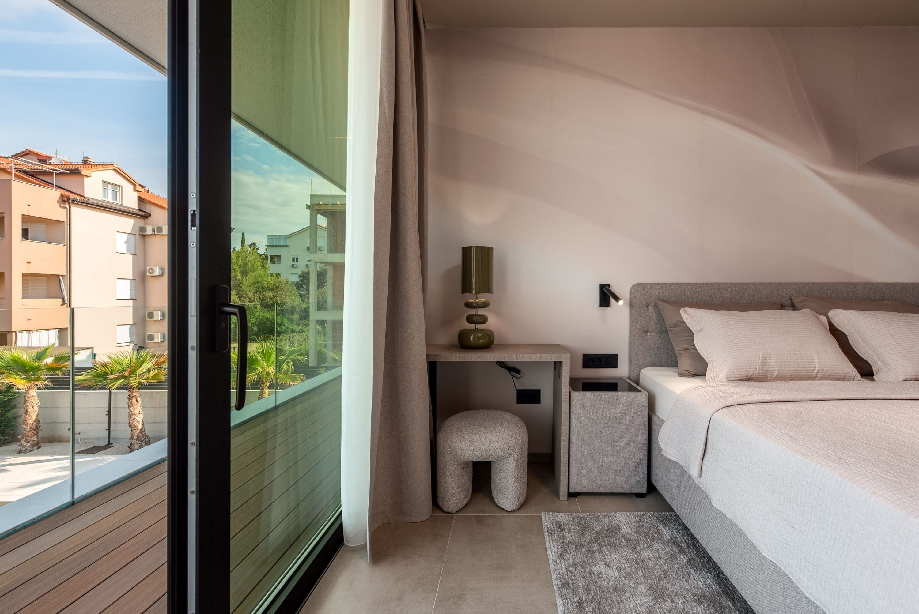 Un dormitorio con cama, mesita de noche, lámpara y vistas a edificios.