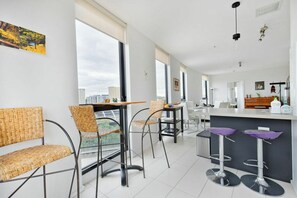 A modern interior with wicker chairs, a bar area, and large windows. - Stylish2BD Penthouse Panoramic Views Nth Melbourne (North Melbourne)