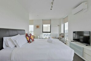 A hotel room with a large bed, a flat-screen TV, a desk with a chair, and a window with a city view. - Stylish2BD Penthouse Panoramic Views Nth Melbourne (North Melbourne)