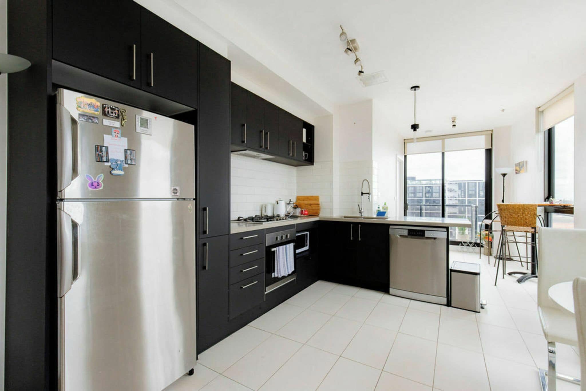A modern kitchen with a stainless steel refrigerator, black cabinets, a built-in oven, and a dishwasher.
